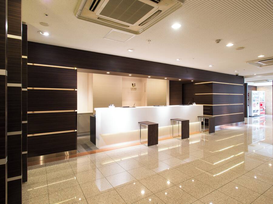 Uma área de recepção moderna com balcão branco, painéis de madeira escura e piso revestido de azulejos.