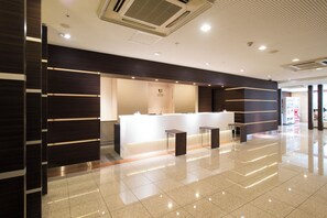 A modern reception area with a white counter, dark wood paneling, and a clean, tiled floor. - JR WEST GROUP VIA INN SHINOSAKA WEST (Osaka)