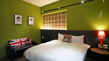 A hotel room with a bed, a bedside table with a lamp, a chair with a Union Jack pillow, and two framed pictures on the wall.