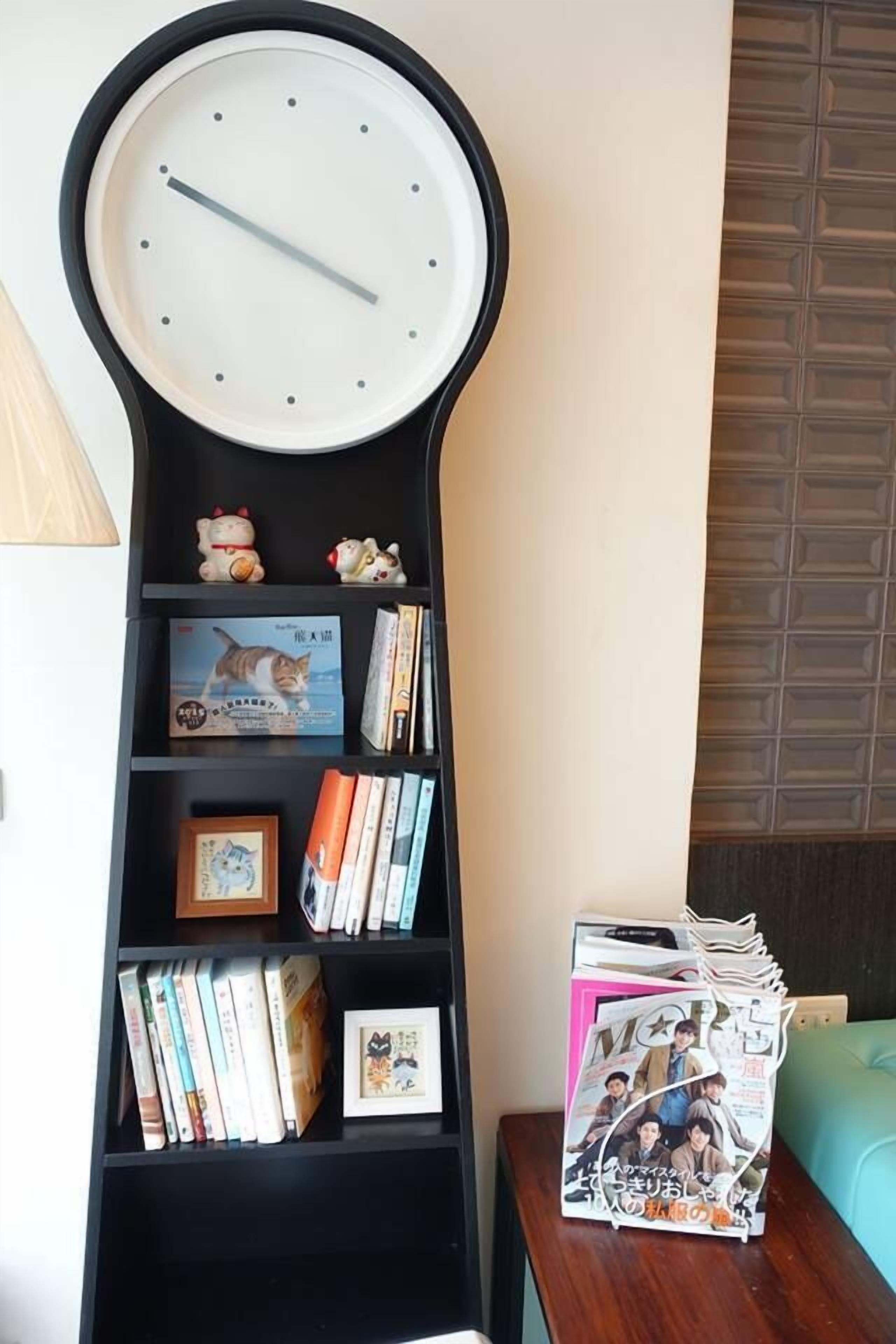 A tall, black bookshelf with a clock on top, filled with books, small figurines, and a magazine.