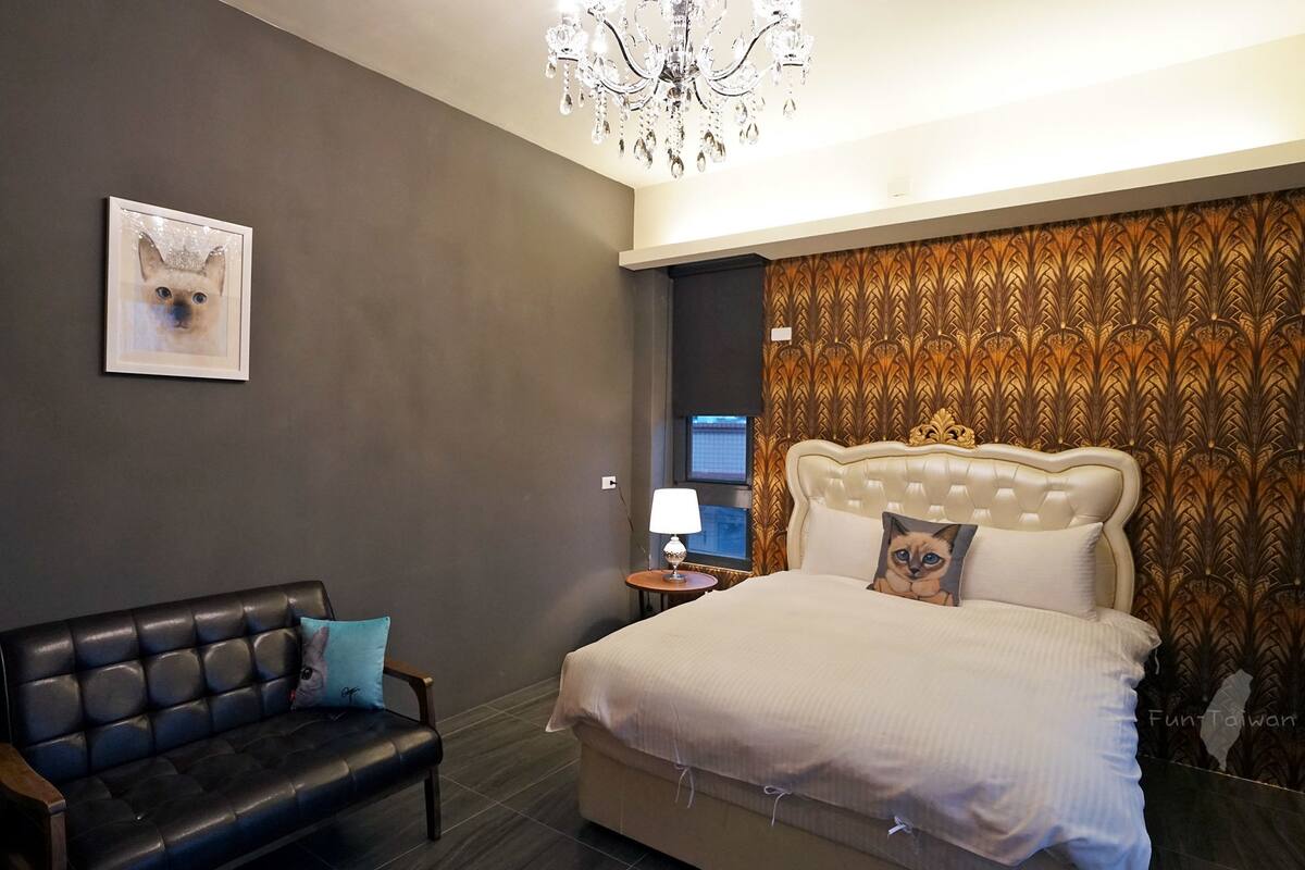 Una habitación de hotel moderna con un sofá de cuero, una cama grande con cabecera acolchada, una araña y papel tapiz estampado.