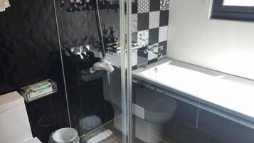 A modern bathroom with a glass shower enclosure, a white sink, and a black and white tiled backsplash.