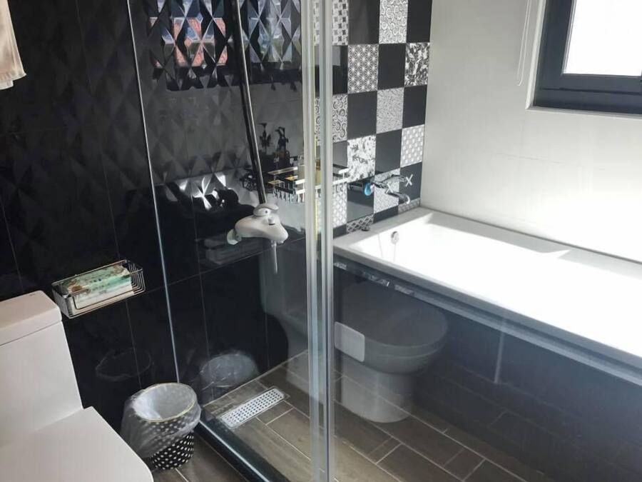A modern bathroom with a glass shower enclosure, a white sink, and a black and white tiled backsplash.