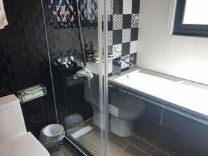 A modern bathroom with a glass shower enclosure, a white sink, and a black and white tiled backsplash.
