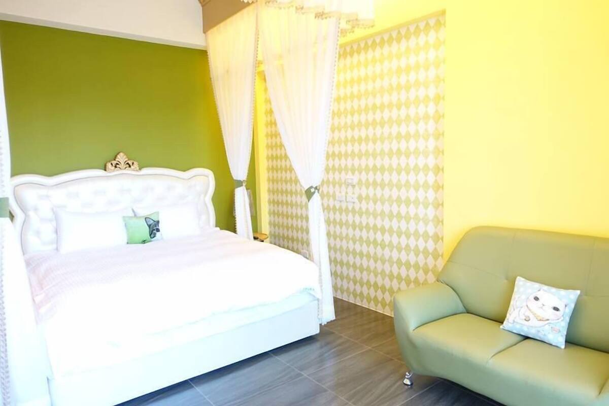 Un dormitorio con cama, sofá verde y cortina estampada.