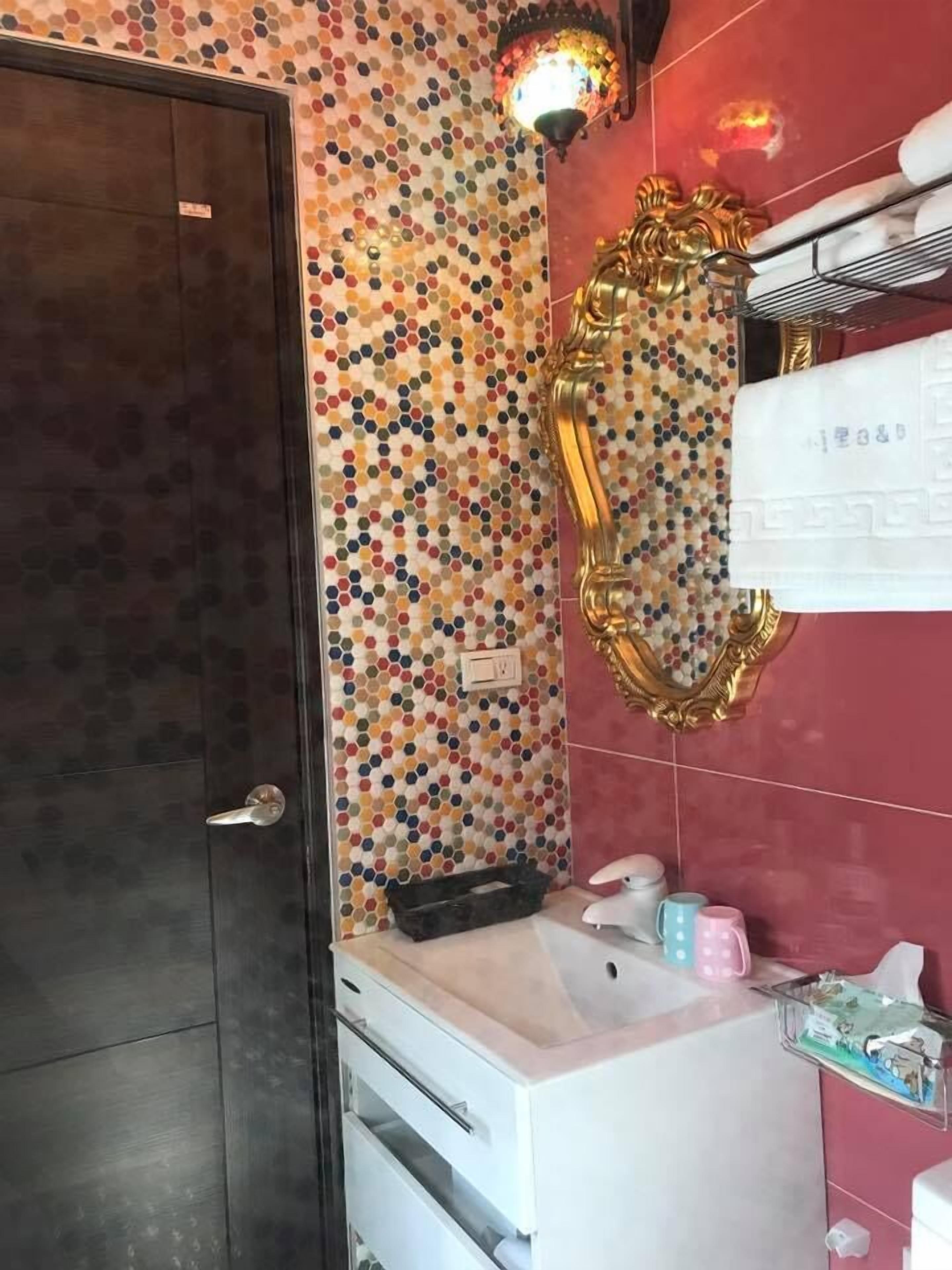A bathroom with a mosaic tile wall, a gold-framed mirror, a white sink, and a dark door.
