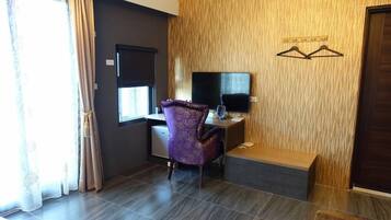 Una habitación con escritorio, silla y televisor. Se ve una ventana con cortinas y un panel de pared de madera.