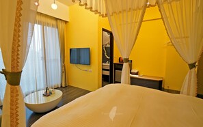 A hotel room with a bed, a round table with a bowl, a TV, and a bathroom visible through an open door.