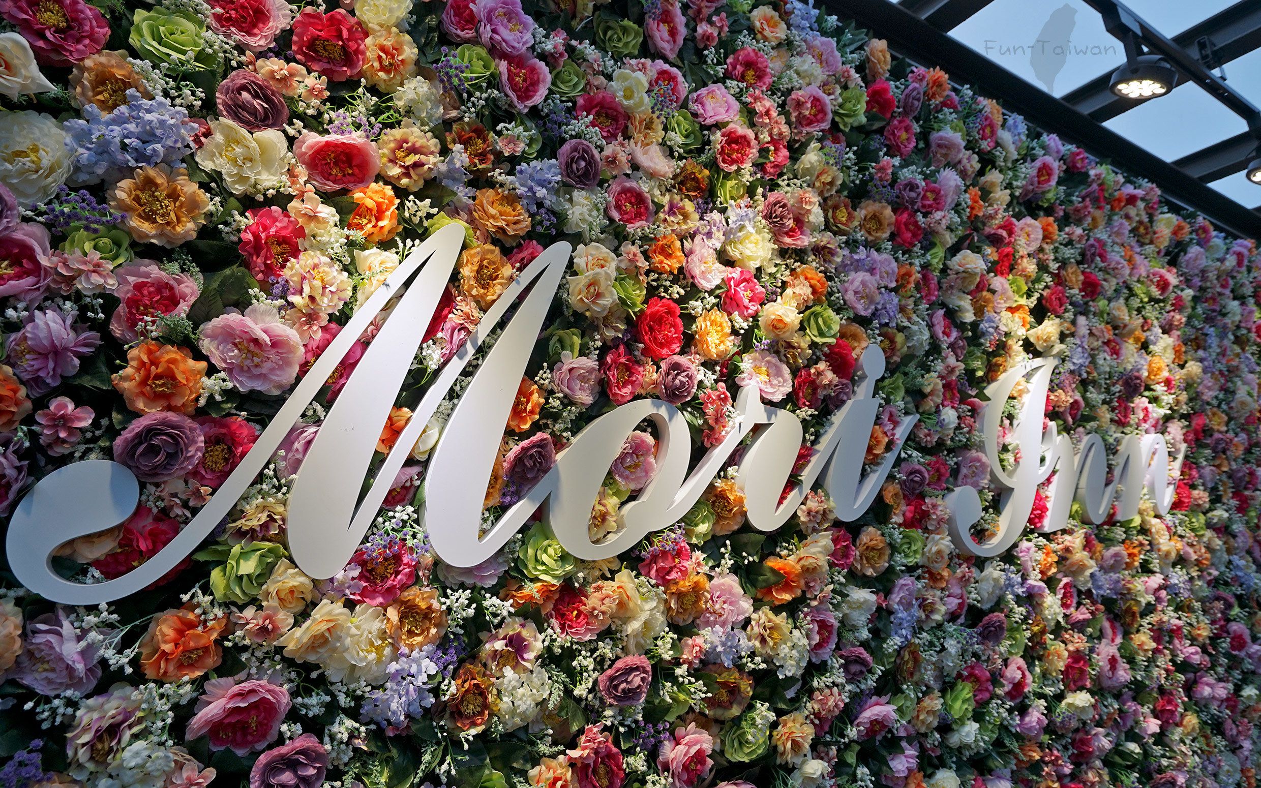 A wall of flowers spelling out "Moyamoya" with a large white sign in the center.