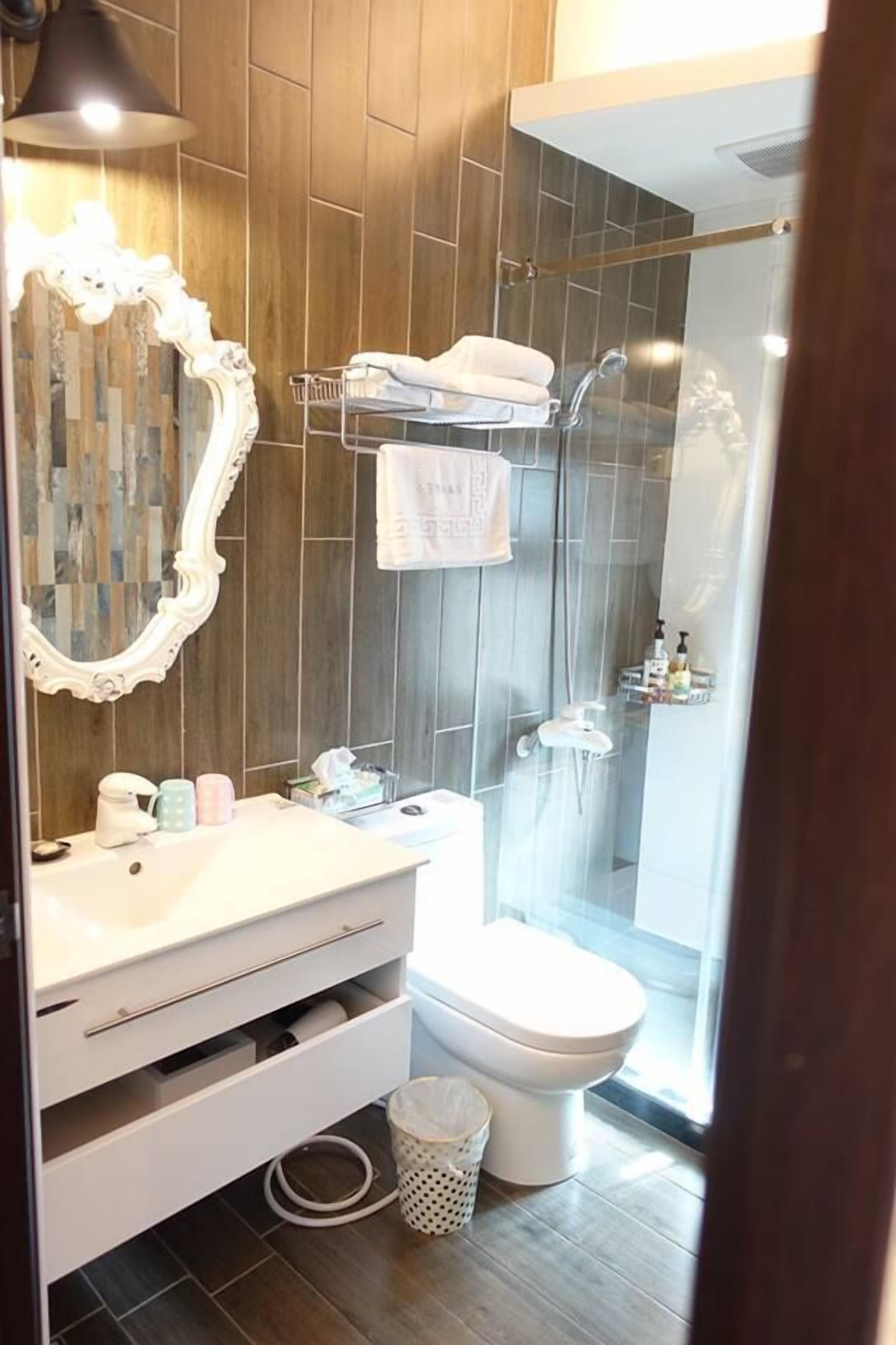 Ein Badezimmer mit Holzwand, einem weißen Waschtisch mit Spiegel, Toilette und Duschbereich.