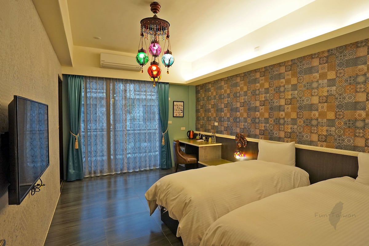 Habitación de hotel con dos camas, un escritorio, un televisor y un papel tapiz decorado.