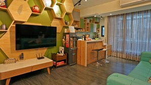 Una sala de estar moderna con un televisor de pantalla plana, estanterías de madera, un sofá verde y una zona de cocina con barra.