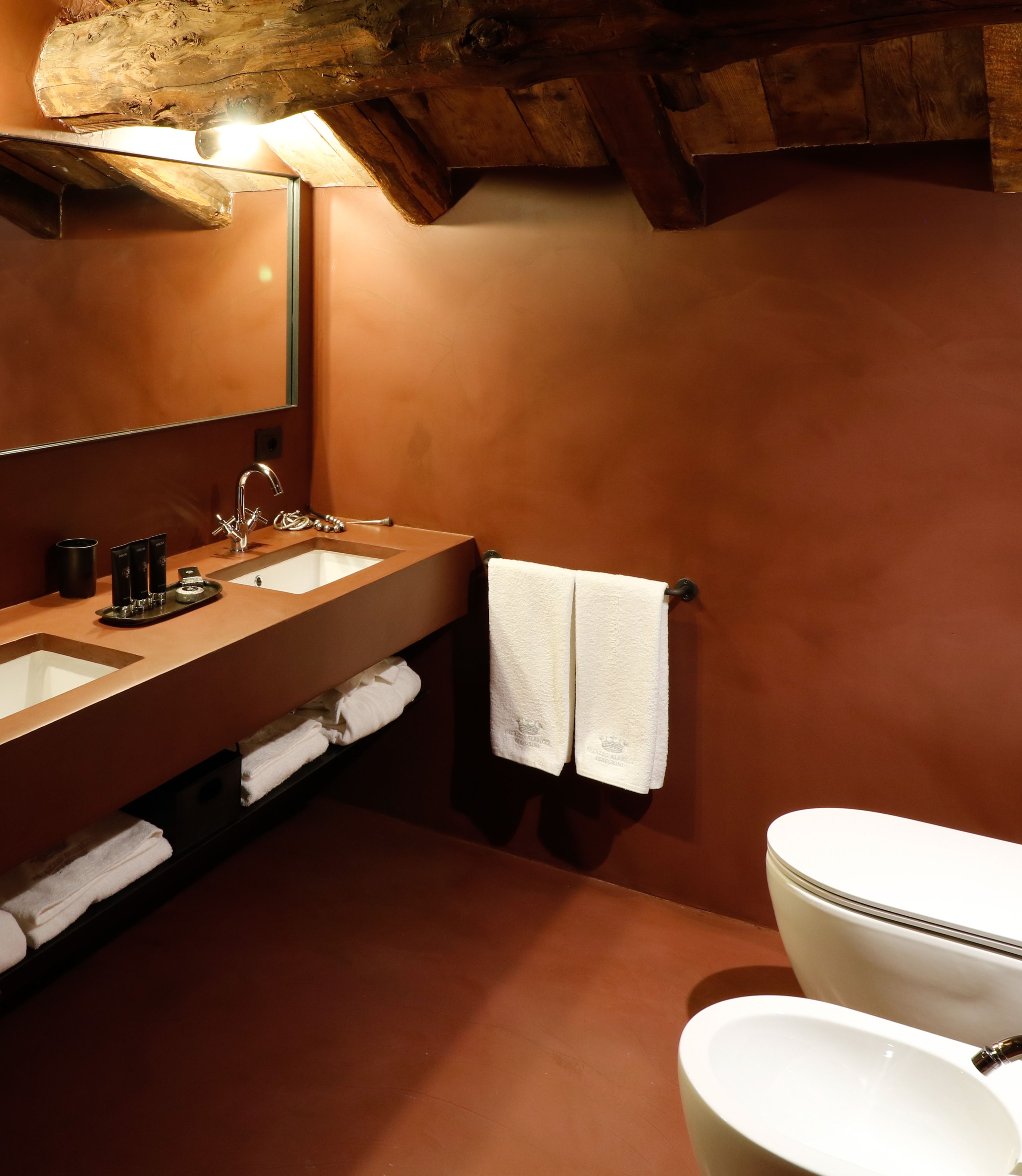 A bathroom with a wooden ceiling, a large mirror, a sink with a faucet, and a toilet.