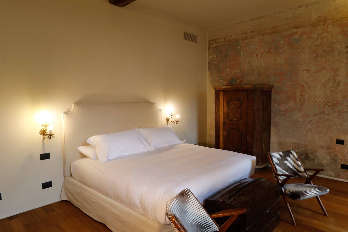 Un dormitorio con una cama grande, dos lámparas de pared, un armario de madera y una silla.