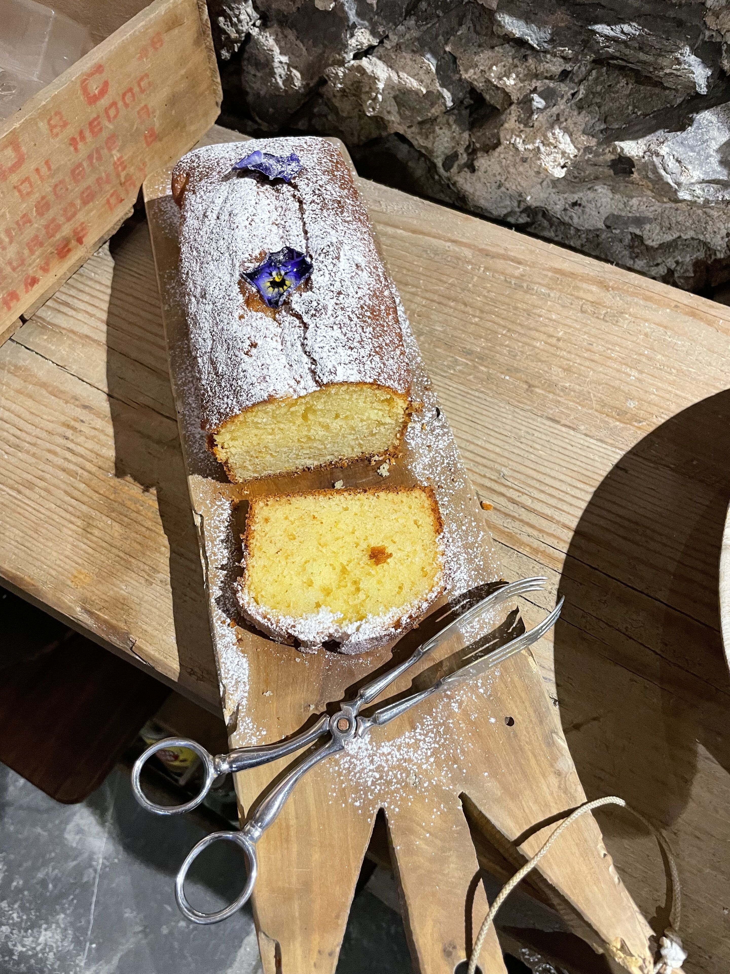Ett brödlimpa med en skiva utskuren, beströdd med florsocker, placerat på en träskärbräda.