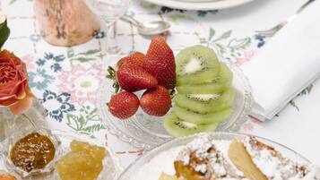 Une table dressée avec une nappe à motifs floraux, sur laquelle on trouve une assiette de tranches de kiwi, des fraises et un dessert saupoudré de sucre glace.