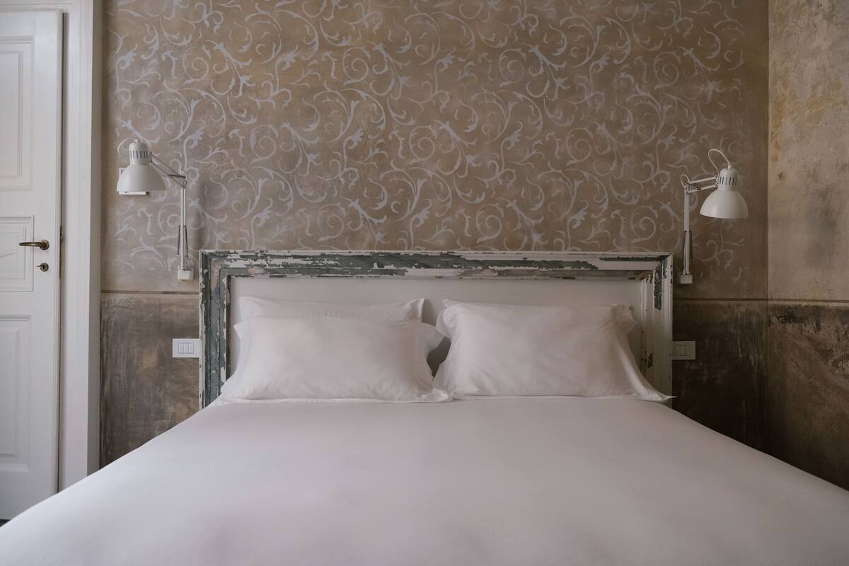 Una cama con sábanas blancas, un papel tapiz estampado y dos lámparas de noche.