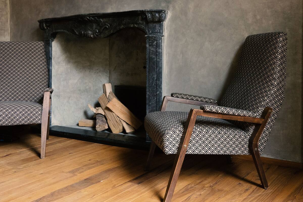 Una habitación con chimenea, dos sillones estampados y suelo de madera.