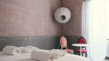 Una habitación de hotel con una cama, dos sillas, una mesita y una lámpara fijada a la pared.