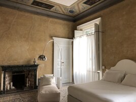 Ein Schlafzimmer mit einem Bett, einem Nachttisch, einer Lampe, einem Kamin und einer Tür.