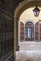 Ein schmiedeeisernes Tor mit aufwendiger Verzierung, das zu einem Gebäude mit einem steinernen Bogen und einer hängenden Laterne führt.
