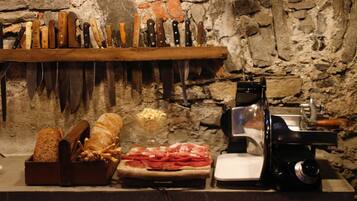 Una cocina con pared de piedra, repisa de madera con cuchillos, un cortador de carne y una cesta de pan.