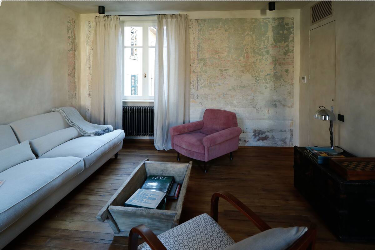 Un salón con sofá, un sillón rosa, una mesa de centro de madera con un libro y un radiador.