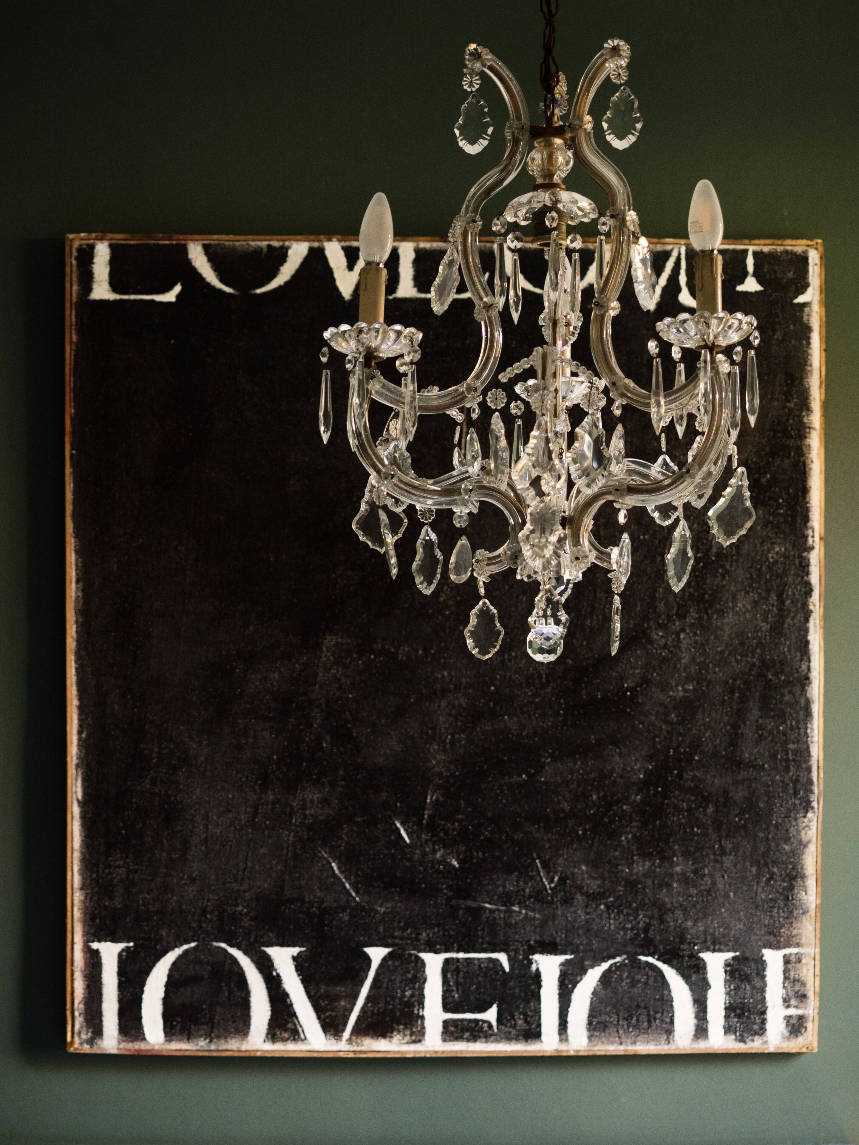 Um candelabro pendurado acima de uma placa com as palavras "LOVE" e "IOVEIOLI" sobre um fundo escuro.