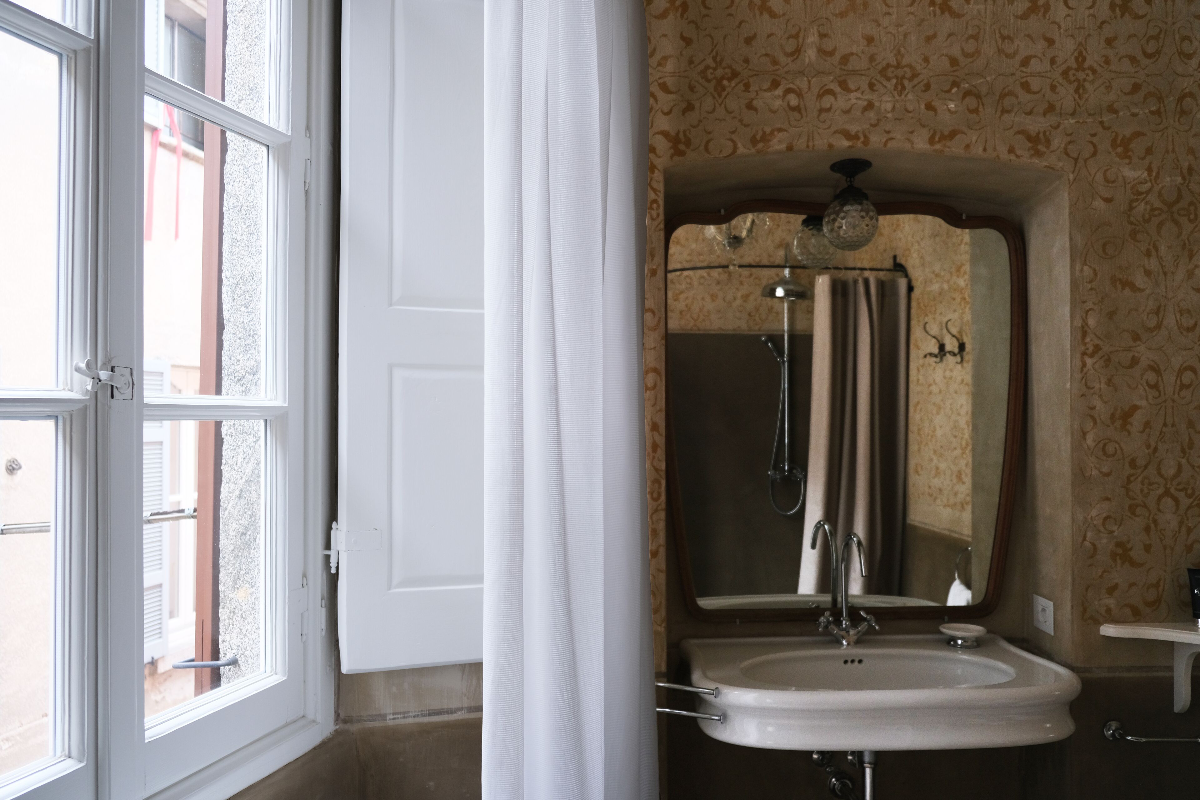 A bathroom with a large window, a sink, a mirror, and a shower.