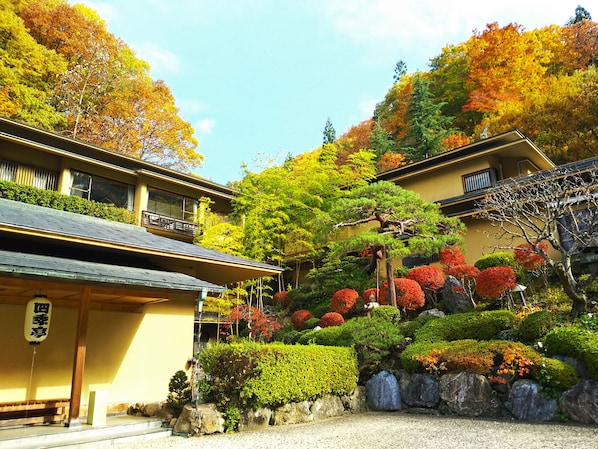 Un edificio japonés tradicional con tejado de tejas, rodeado de jardines cuidados y árboles de colores otoñales.