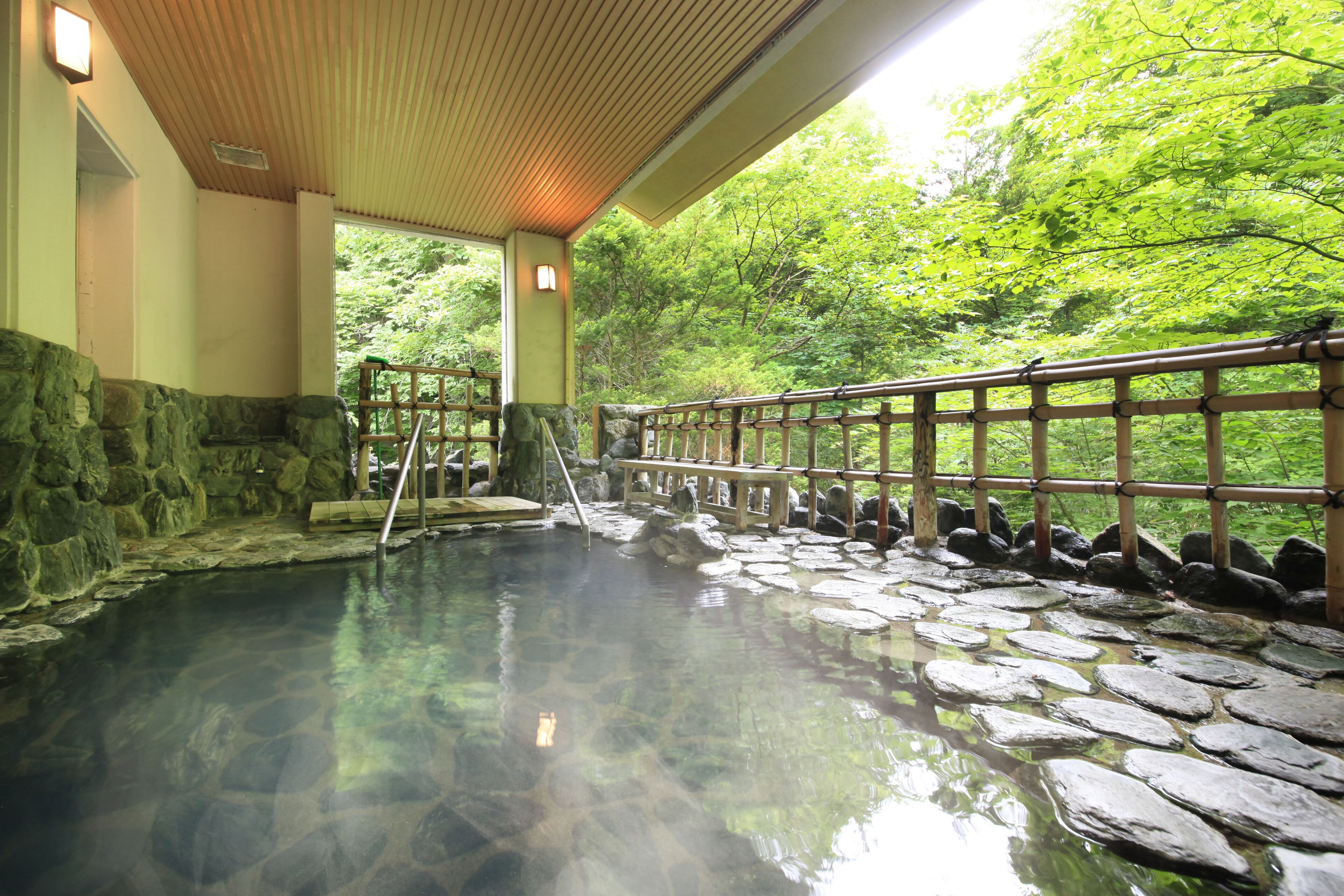 A traditional Japanese onsen with stone flooring, wooden railings, and a view of lush greenery outside.