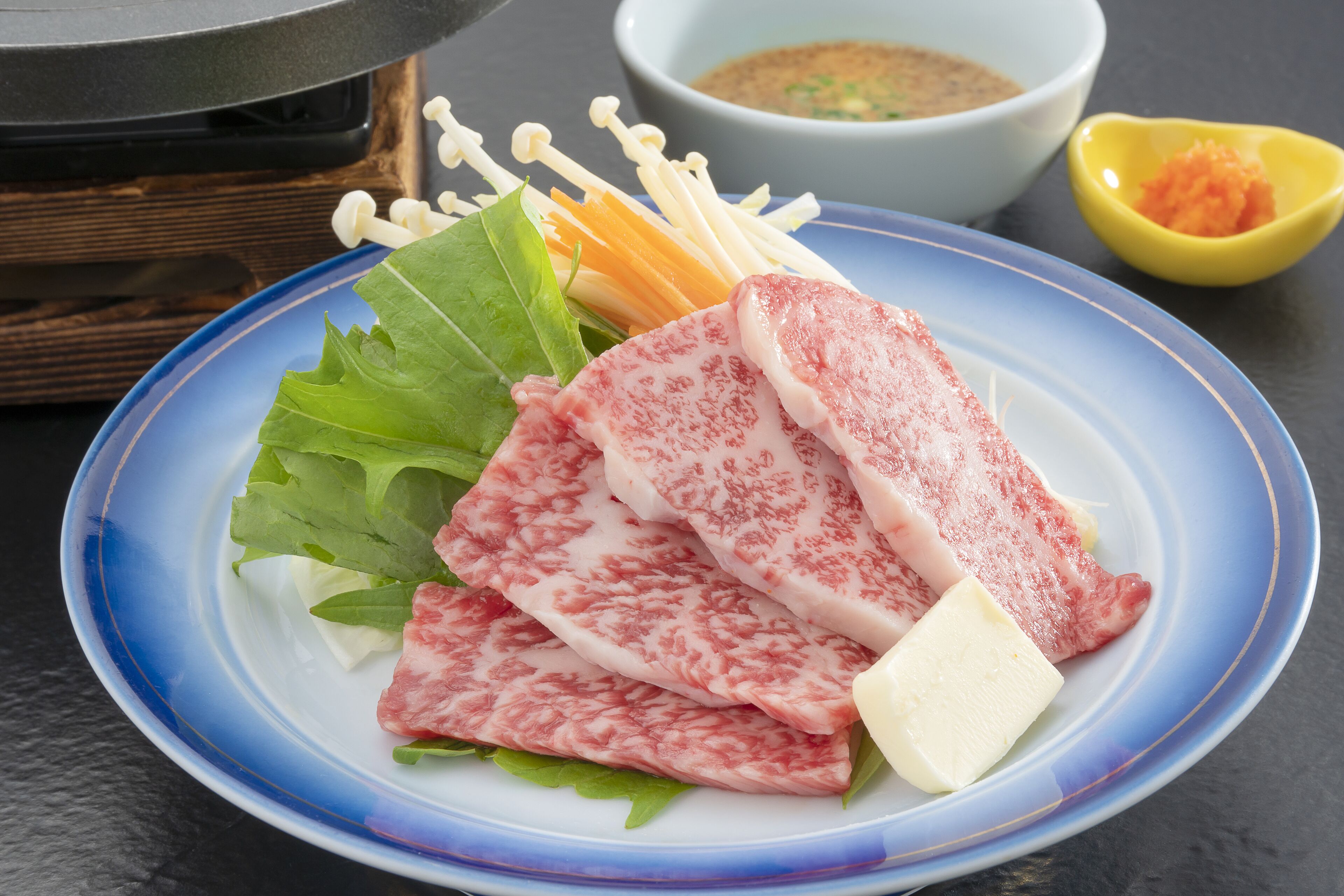 A plate with sliced meat, vegetables, and a small bowl of sauce.