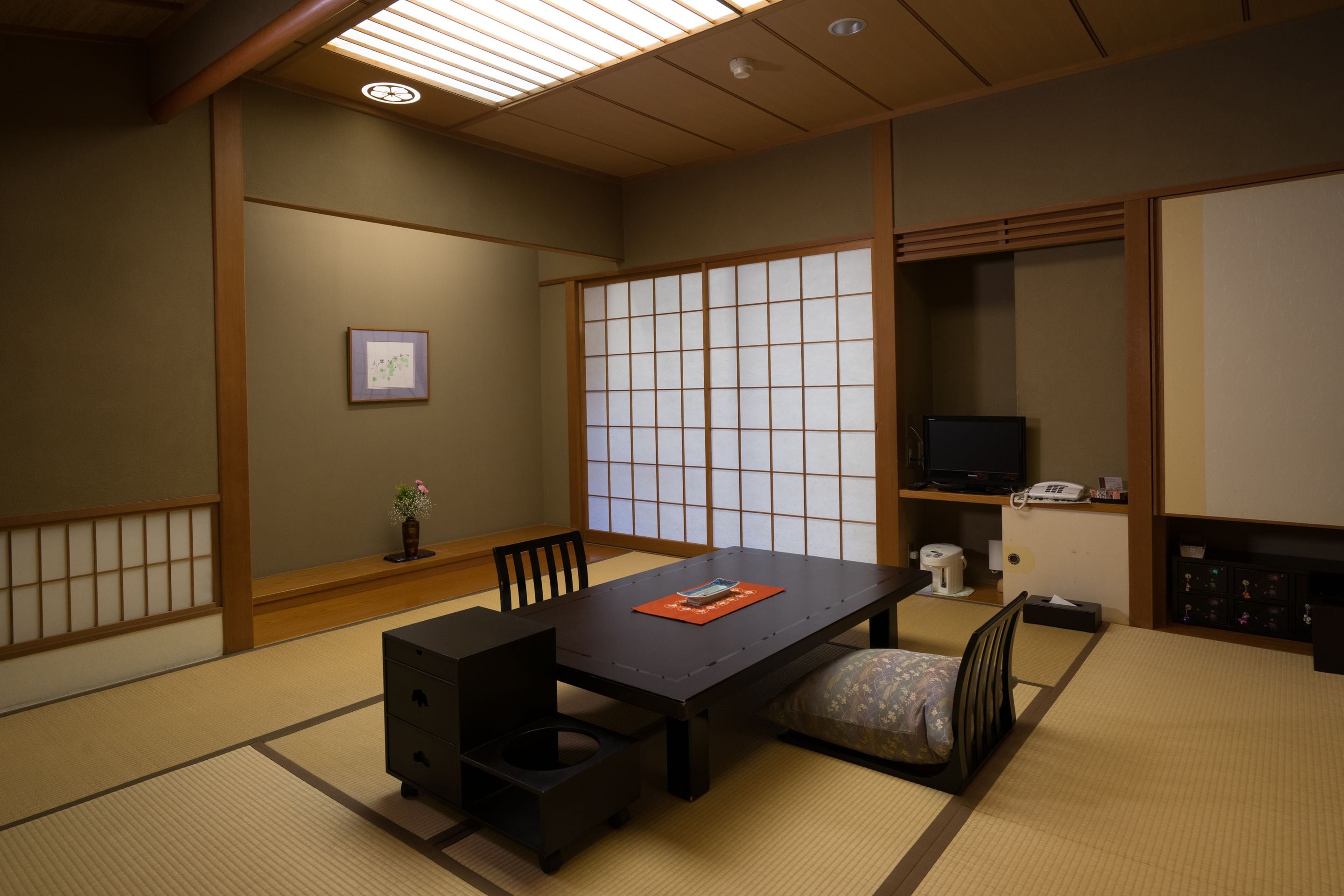 Una habitación japonesa tradicional con suelo de tatami, una mesa baja, un televisor y un armario.