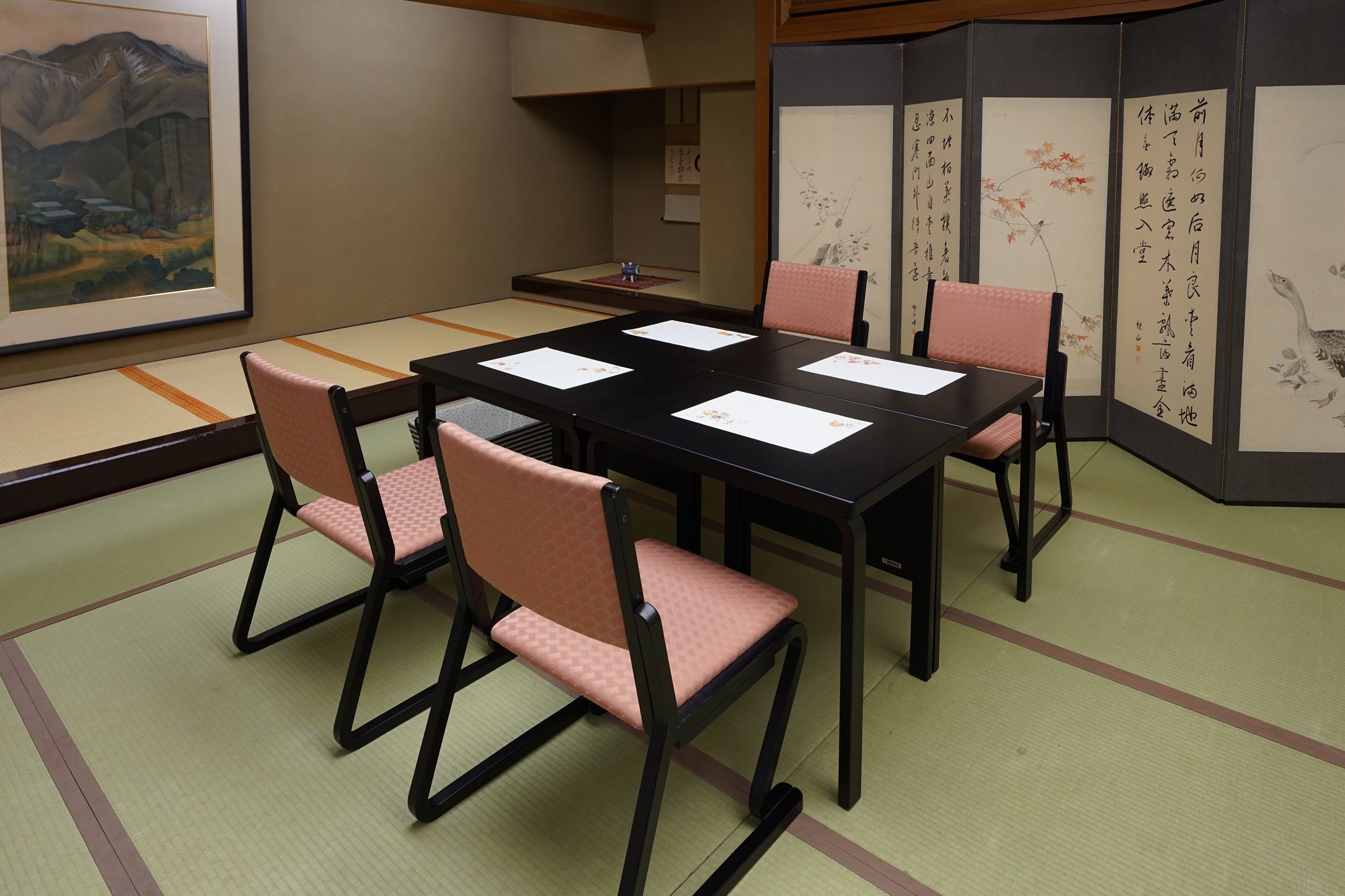 A traditional Japanese room with tatami flooring, a low table with four chairs, and calligraphy on the walls.