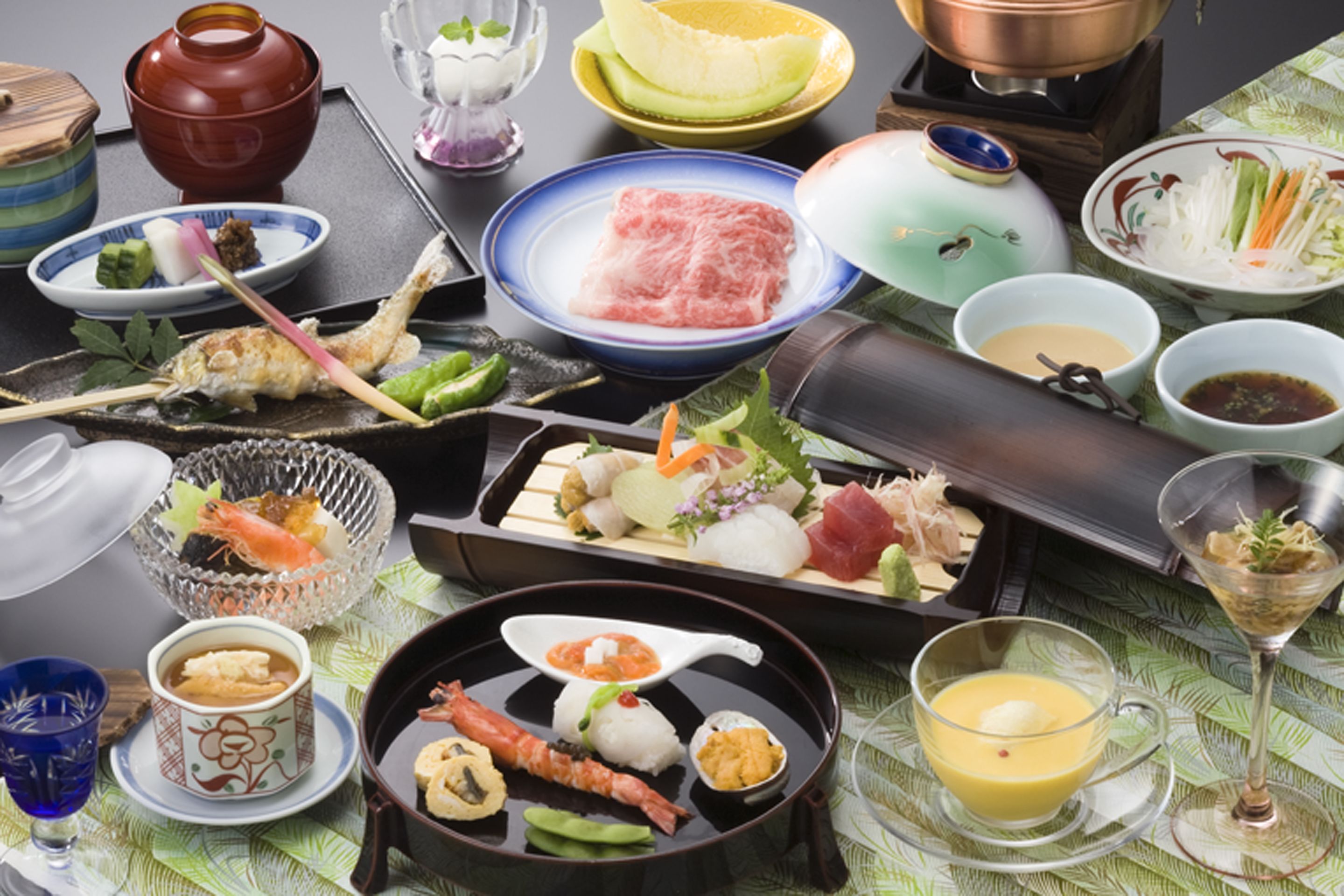 Variedade de pratos e bebidas japoneses sobre uma mesa, incluindo sushi, sashimi e um pote quente.