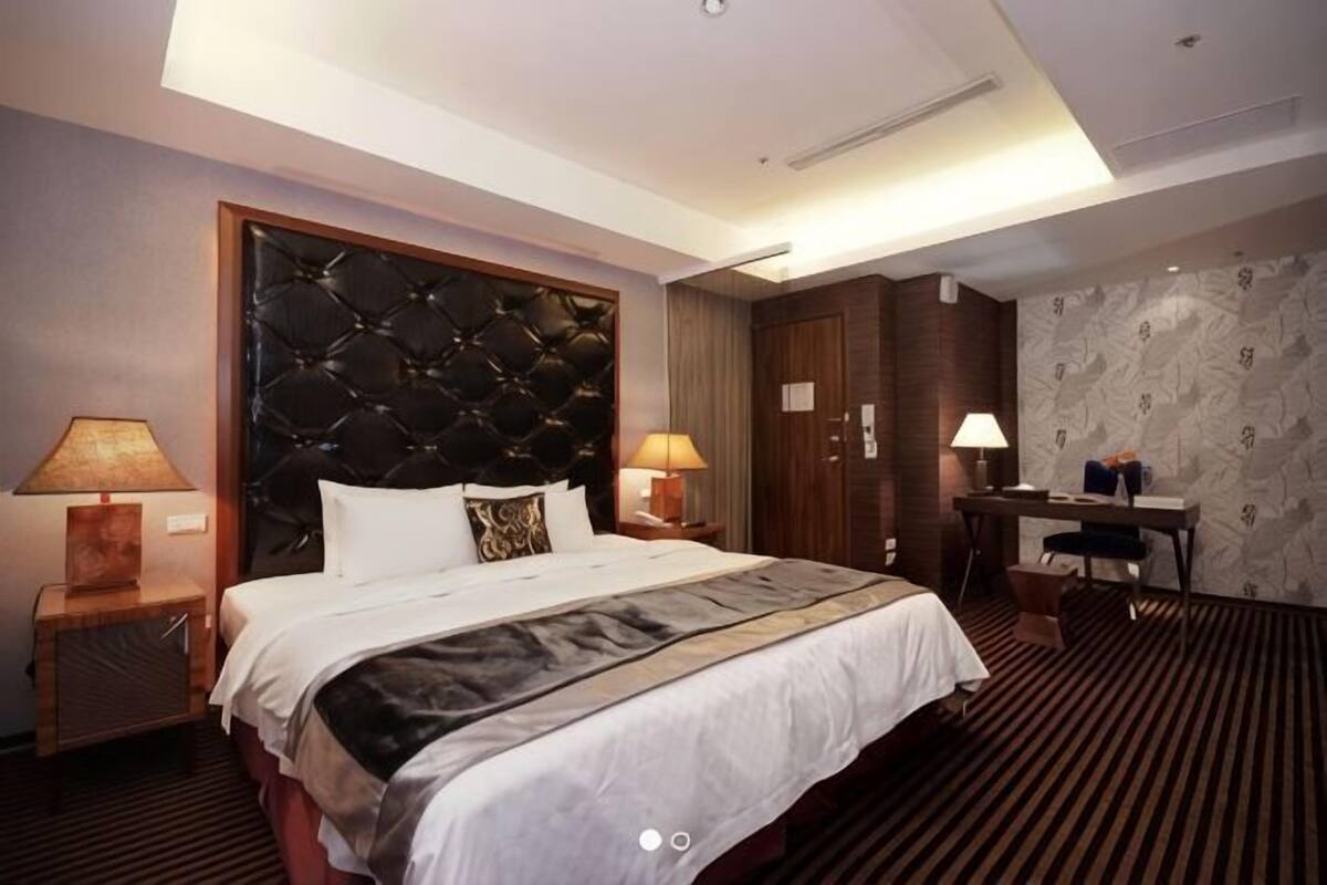 A hotel room with a large bed, two bedside tables with lamps, a desk, and a chair.