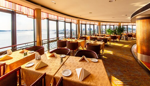 A restaurant with tables set for dining, large windows offering a view of the water, and a curved ceiling design.