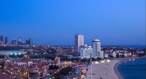 A coastal cityscape with a prominent beach, high-rise buildings, and a mix of residential and commercial structures. - Huiquan Dynasty Hotel (Qingdao)