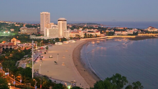 A coastal cityscape with a beach, high-rise buildings, and a promenade. - Huiquan Dynasty Hotel (Qingdao)