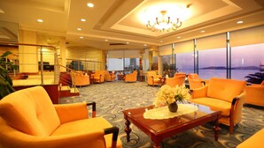 A hotel lobby with orange seating, a glass coffee table with a vase, and large windows offering a view of the sea. - Huiquan Dynasty Hotel (Qingdao)