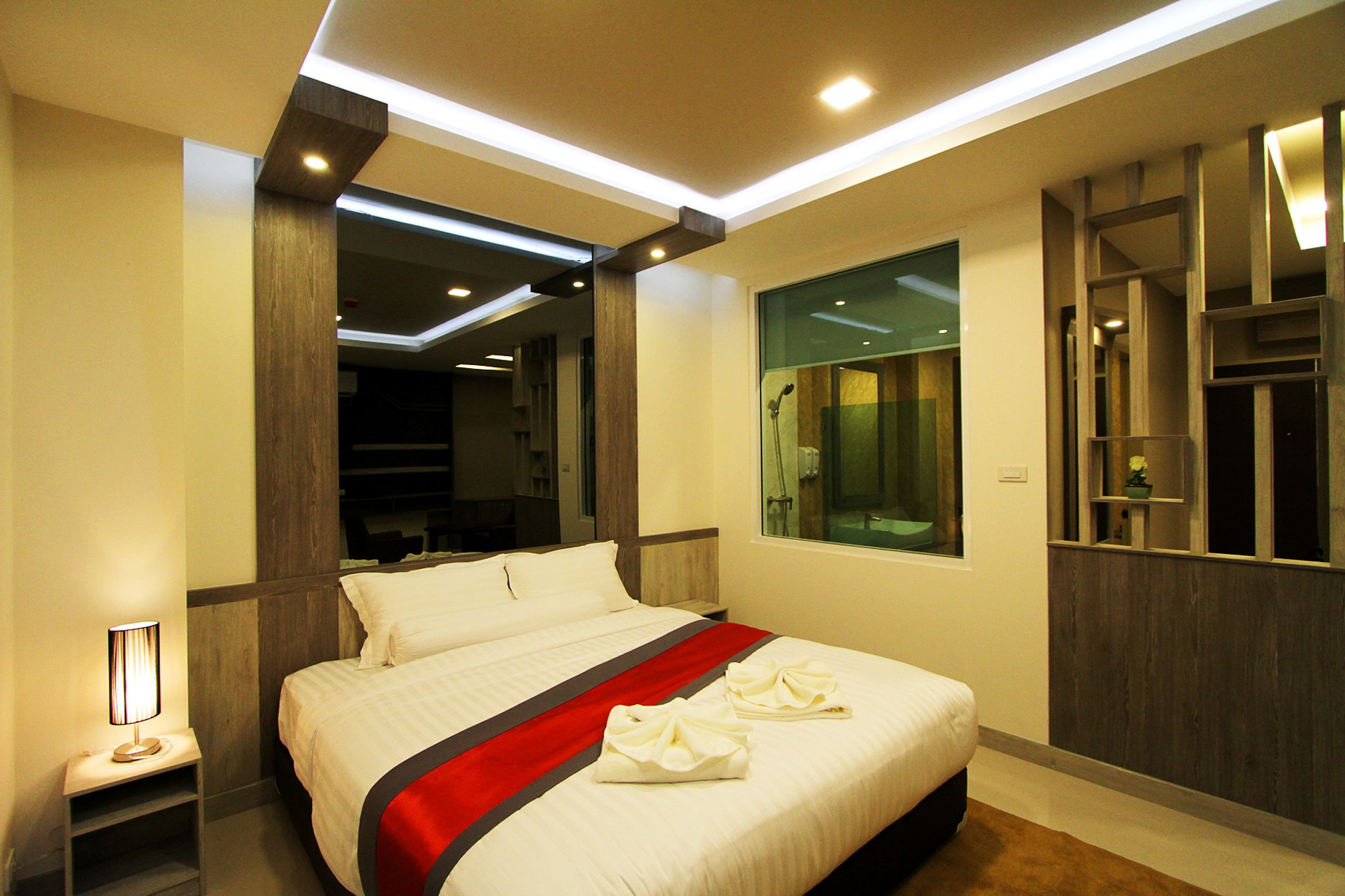 A modern hotel room with a large bed, a bedside table, a mirror, and a window.