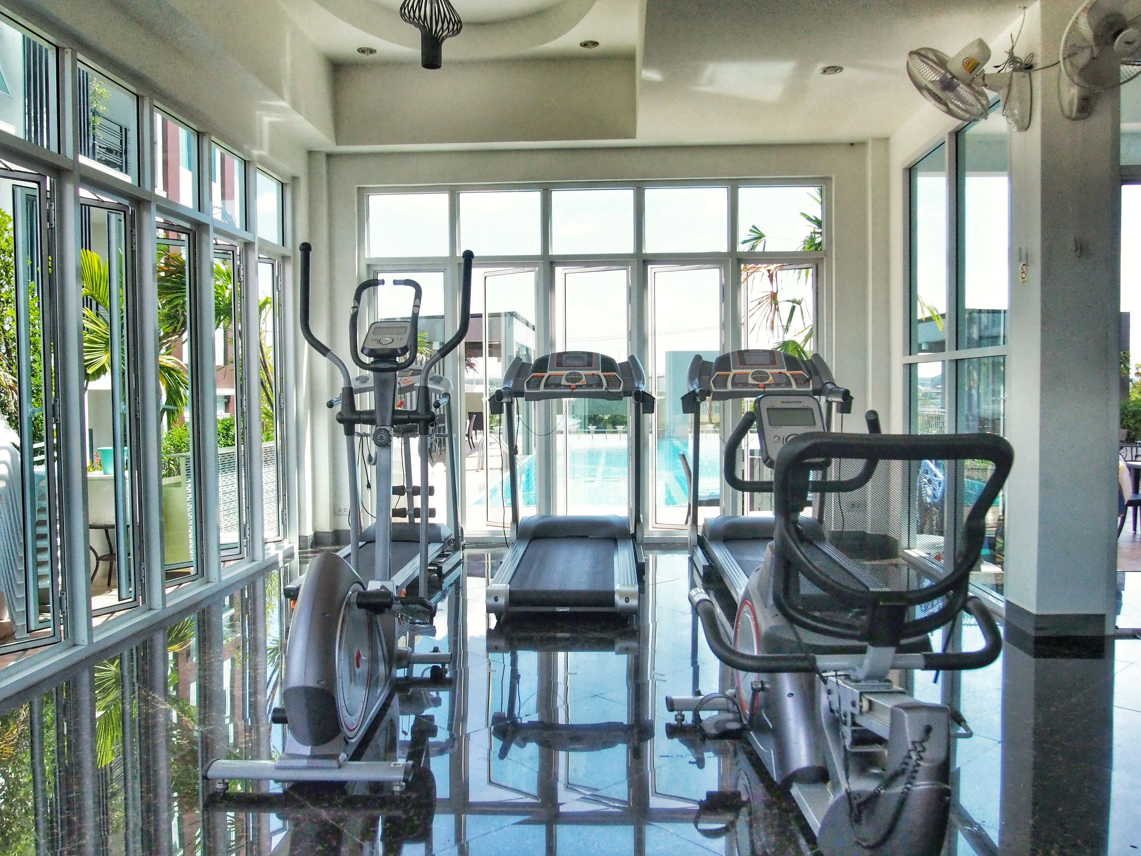 A gym with cardio machines, large windows, and a view of the outdoors.