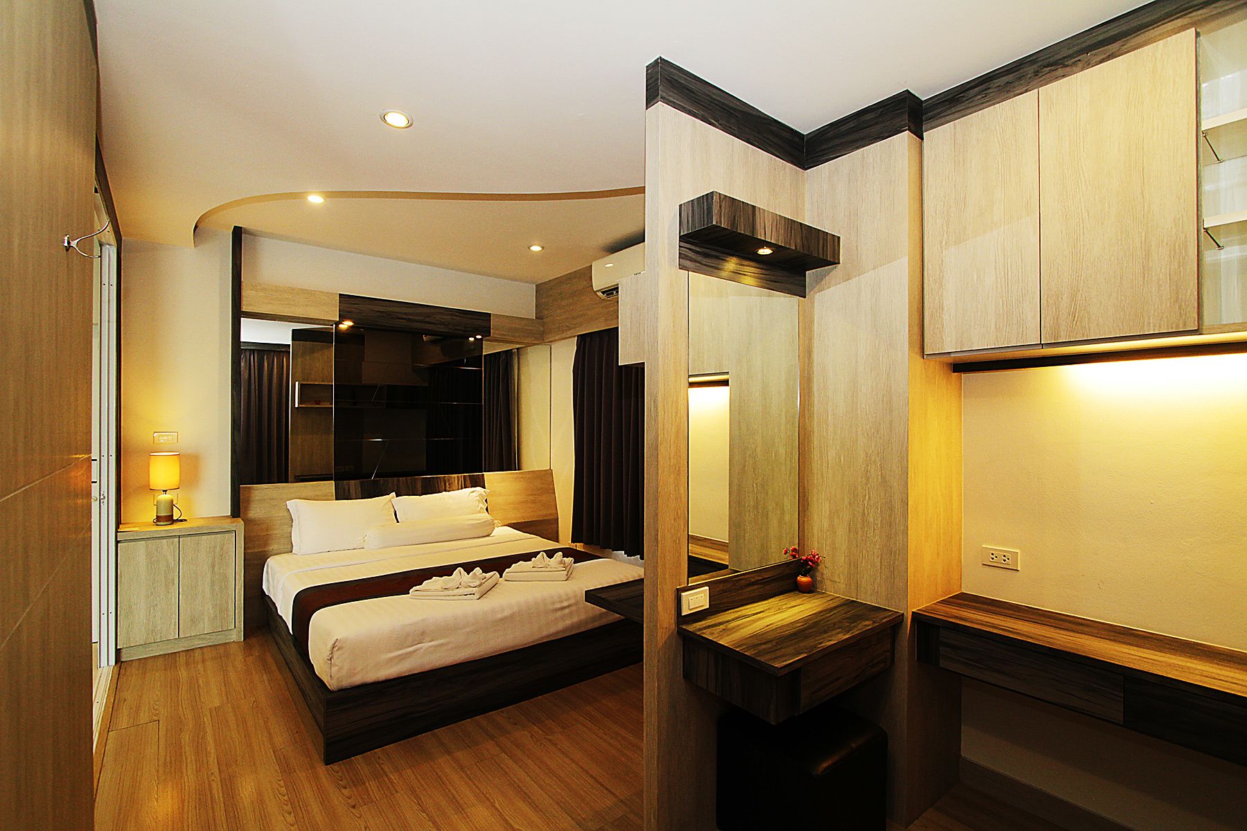 A hotel room with a bed, bedside table, mirror, and wooden flooring.