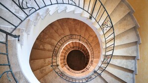 Una escalera de caracol con un espacio abierto en el centro, rodeada de escalones de piedra y barandillas de metal.