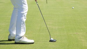 Una persona en un campo de golf, concentrada en una pelota y un palo.