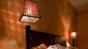 Habitación de hotel con cama, mesita de noche, lámpara, pantuflas y un jarrón con flores.