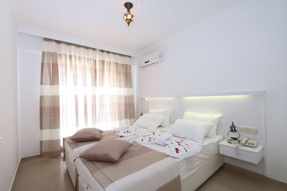 Una habitación de hotel con dos camas, una mesita de noche con teléfono y una ventana con cortinas.