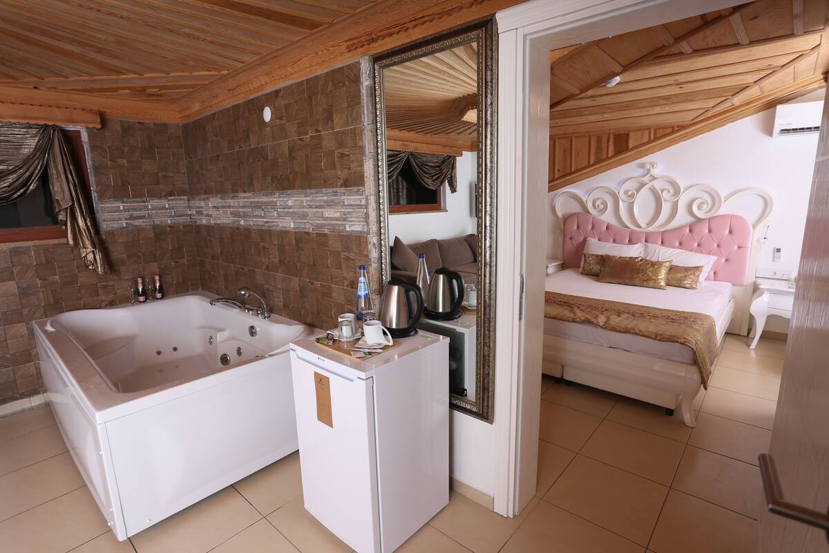 Un baño con una bañera grande, un mueble blanco pequeño y un espejo.