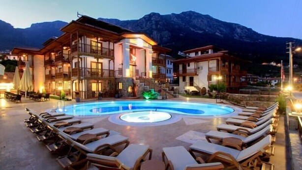 Un hotel con piscina rodeado de sillas de descanso, con montañas al fondo.