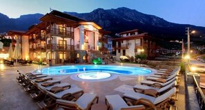 Un hotel con piscina rodeado de sillas de descanso, con montañas al fondo.